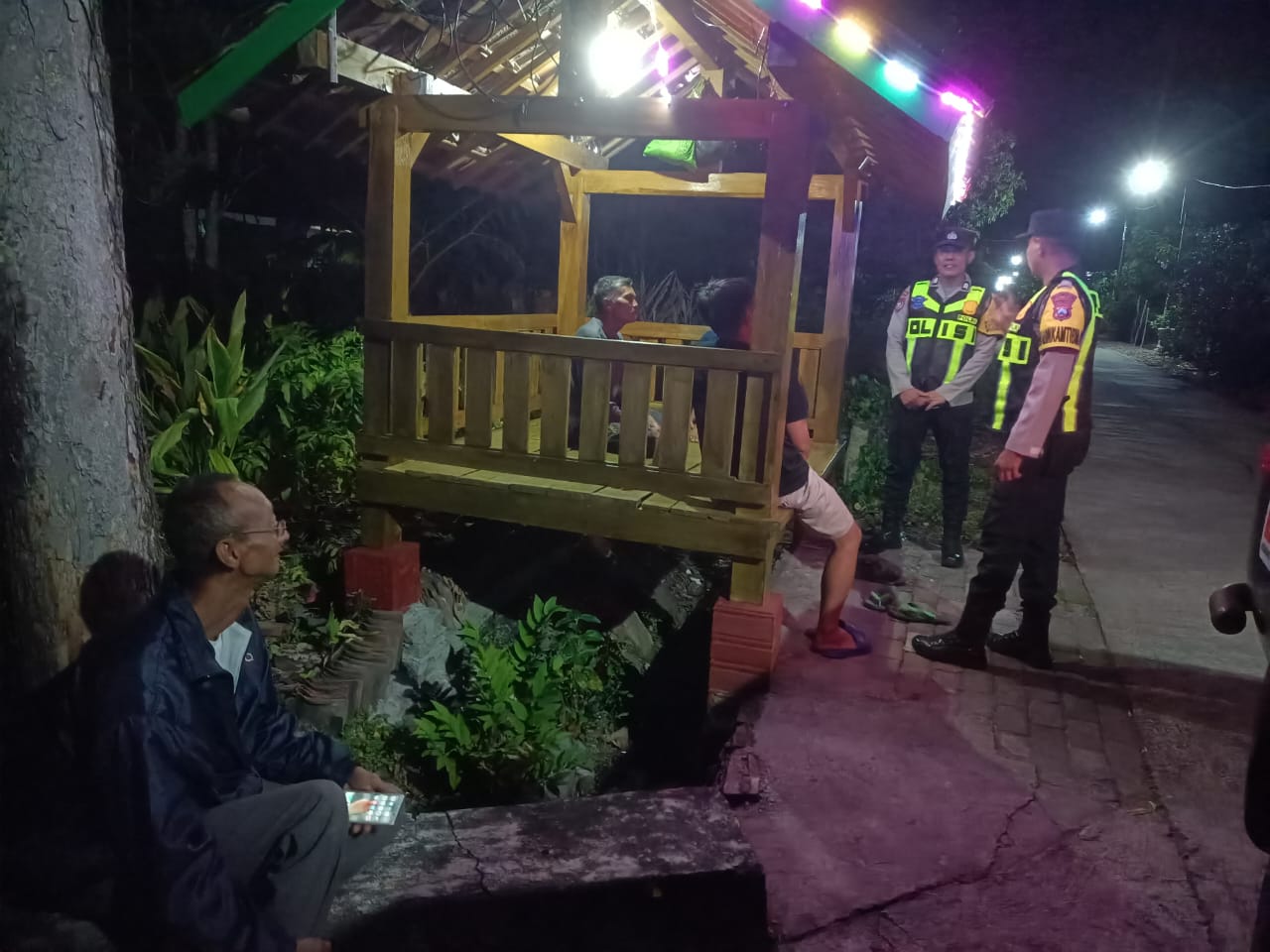 Personil Polsek Lembeyan sambang dan dialogis kepada masyarakat yang berjaga di poskamling guna berikan himbauan Kamtibmas dan ajak warga wujudkan keamanan lingkungan